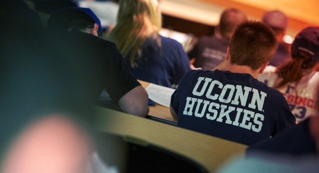 UConn students listening a in lecture. One student wears a shirt with UConn Huskies screen printed in the center.